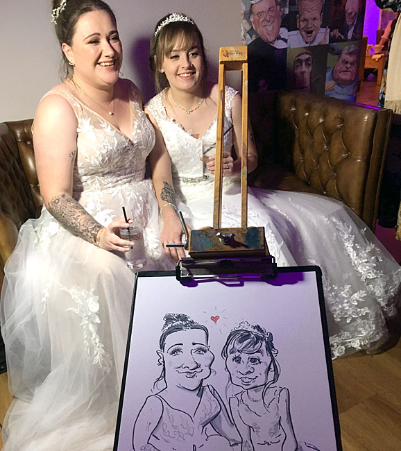 photo showing two brides at their barn wedding in worcestershire with caricature drawing on easel